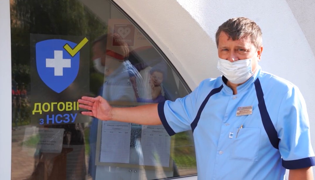 Медик навів руку на двері з наліпкою про співпрацю аптеки із НСЗУ.